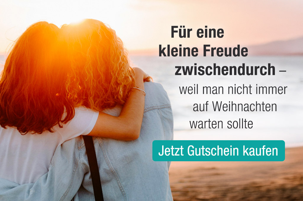 Zwei Personen umarmen sich am Strand bei Sonnenuntergang. Text: "Für eine kleine Freude zwischendurch... Jetzt Gutschein kaufen."